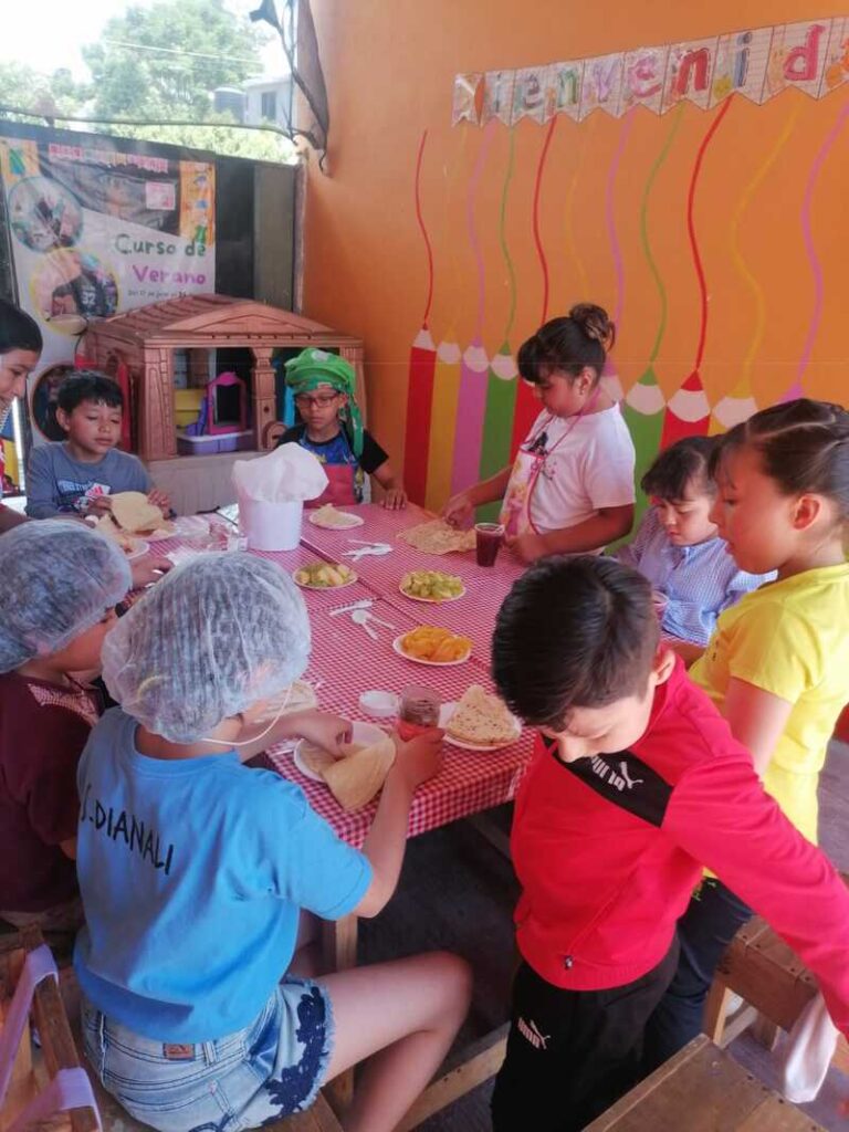 NIños con boina cocinando pizza en una mesa