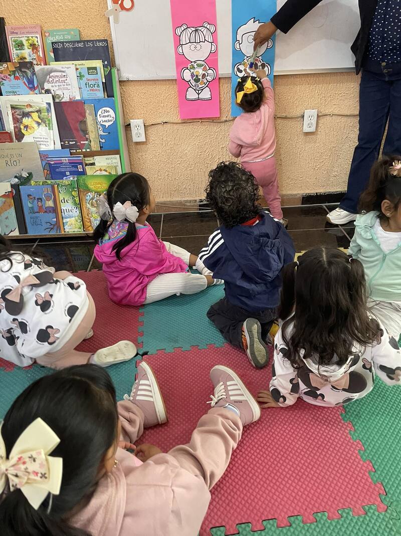 niños pequeños sentados viendo a una de sus compañeras pegar algo en la pared